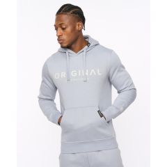 Man wearing a light grey hoodie with "ORIGINAL" text. He looks to the side, hands in pockets, against a plain white background. Casual and relaxed vibe.