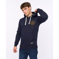 Young man in a navy hoodie with tan accents, adjusting his hood. The hoodie has a front pocket and circular text design, paired with blue jeans.