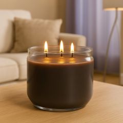 Three-wick dark amber candle burning in a clear glass jar on a wooden coffee table in a cozy living room setting