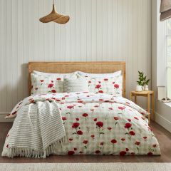 Cozy bedroom with a rattan headboard, white bedding patterned with red poppies, and a fringed throw, lit softly beside a potted plant.