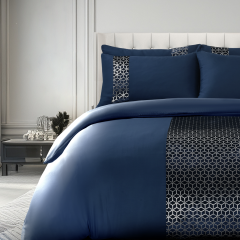 Elegant bedroom with a navy blue duvet cover set featuring a geometric pattern, flanked by matching pillows, in a softly lit, modern room.