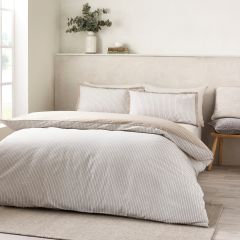 Bright, serene bedroom with a neatly made bed in striped beige bedding, greenery on a shelf, soft sunlight, and neutral decor.