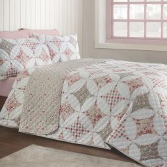 Pastel floral patchwork quilt drapes over a bed in a bright bedroom, beside a pink-trimmed window, creating a soft, cozy atmosphere.