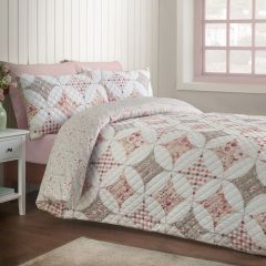 Cozy bedroom with a pastel floral patchwork quilt on a pink bed, beside a sunlit window; soft colors create a calm, welcoming mood.