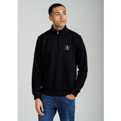 Man wearing a black quarter-zip sweater with white embroidery on the chest, paired with blue jeans. He stands against a plain background, looking to the side.