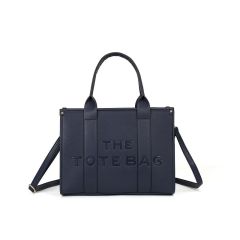 Navy blue tote bag with "The Tote Bag" embossed on the front. It has two short handles, a shoulder strap, and a minimalist design.