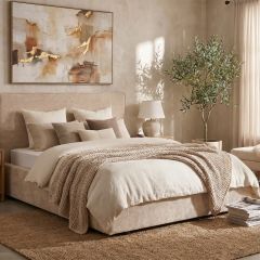 Beige upholstered bed with neutral bedding in a warm contemporary bedroom setting.