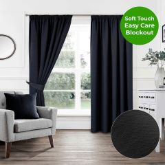 Black soft touch blockout pencil pleat curtains styled in a bright modern living room with grey armchair