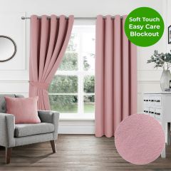 Blush pink blackout eyelet curtain hanging on a silver curtain pole against a white wall