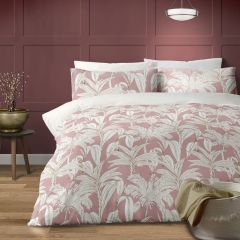 A cozy bedroom scene features a bed with a duvet and pillows adorned in a white palm leaf pattern against a pink background. The room has a warm wooden floor, a maroon paneled wall, a round side table with a potted plant, and a modern pendant light overhe