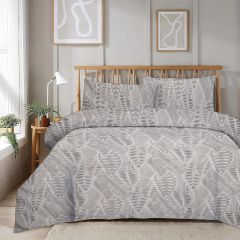 Bedroom with a wooden bed frame, gray leaf-patterned bedding, abstract wall art, a small plant, and a window with soft light.