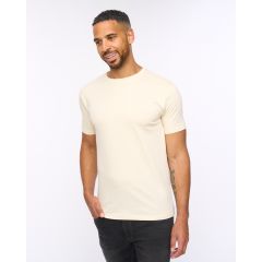 Man wearing a beige t-shirt and black jeans, smiling with a relaxed posture against a plain white background. Casual fashion, confident mood.