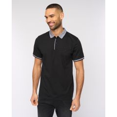 Man smiling in a black polo shirt with white trim, standing against a plain background. His relaxed pose conveys a casual, cheerful vibe.