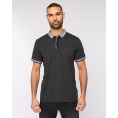 A man in a charcoal polo shirt with a white-trimmed collar and sleeves stands against a plain background. He appears confident and composed.