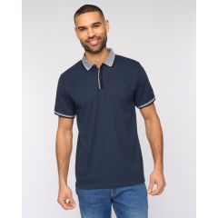 A man in a navy polo shirt with a white-trimmed collar and sleeves stands against a plain background. He appears confident and composed.