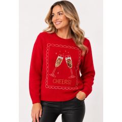 A woman wearing a red knitted holiday jumper featuring a sequin champagne glass graphic and an embroidered "CHEERS!