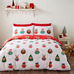 Festive bedding with cute cartoon robins in holiday attire against a white background. A shelf above holds red decorations, gifts, and warm lights. Cozy, cheerful scene.