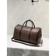 Brown checkered duffel bag with dark leather straps and a shoulder strap on a white textured surface, against a light tiled wall.