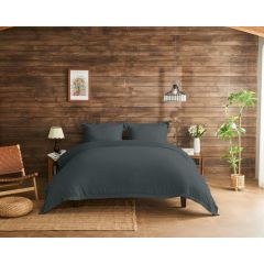 Inviting bedroom with charcoal bedding on a wooden bed, against a rustic wood-paneled wall. Decor includes a woven chair, plants, and soft lighting.