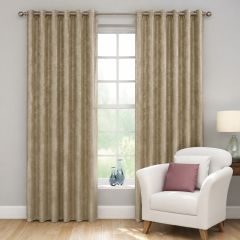 Gold Mayfair eyelet curtains framing a tall window beside a cream armchair.
