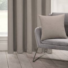 A minimalist room features beige curtains, a soft gray chair, and a matching light beige pillow. The mood is calming and elegant, with natural light.