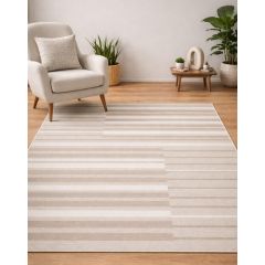 A cozy living room with a beige armchair and textured cushion on a hardwood floor. A striped beige rug is in the foreground, flanked by green plants.