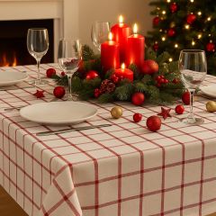 Christmas dining table decorated with a red and white plaid tablecloth, festive candles, baubles, and evergreen centerpiece