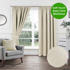 Cream soft touch blockout pencil pleat curtains styled in a bright modern living room with grey armchair