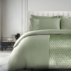 Elegant bedroom with a plush, light green comforter featuring geometric patterns, matching pillows, and a tufted headboard. Modern decor accents.
