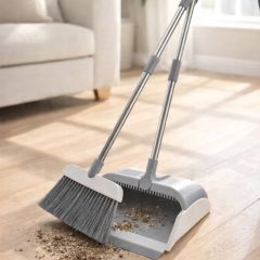Long-handled dustpan and broom set in use on a wooden floor, showing built-in comb teeth on the dustpan for removing debris from the broom head