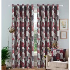 Geometric patterned jacquard curtains in red and grey hang in a cozy living room. A beige armchair with a matching cushion, houseplant, and floor lamp complete the decor.