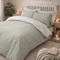 A cozy bedroom with a white wooden bed, sage floral bedding, white pillows, and a light-filled window. Minimalist decor with a serene ambiance.