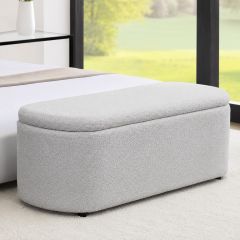 Grey boucle storage bench with a cushioned lift-up lid, upholstered ottoman for bedroom storage positioned at the foot of a modern bed.
