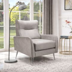 Modern grey velvet armchair with chrome legs in a bright living room setting, styled beside a floor lamp and side table.