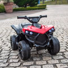 Red and black kids’ ride-on quad bike positioned on cobblestone ground with no rider