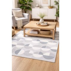 Modern living room featuring a light wood coffee table on a geometric-patterned rug. A cozy armchair, plants, and white sideboard create a serene atmosphere.