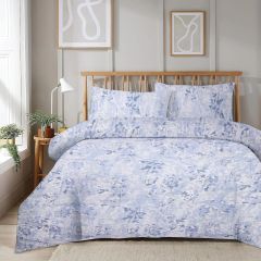Bedroom with a wooden bed featuring blue floral bedding, abstract wall art, a side table with a plant, and a large window with white curtains.