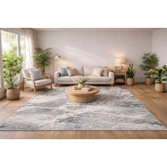 Modern living room with a beige sofa, cushions, and a floor lamp. Wooden coffee table on a gray and blue patterned rug. Surrounded by lush potted plants.