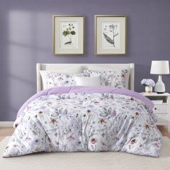 White comforter set with delicate purple floral designs and a solid purple reverse, styled in a modern bedroom.