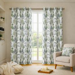 Cozy living room with floral-patterned curtains on a window, an armchair with a matching cushion, a soft rug, and candles on a tray, creating a peaceful ambiance.