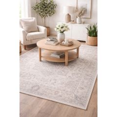 Cozy living room with beige armchair, round wooden coffee table with books and flowers, elegant patterned rug, and plants, creating a serene ambiance.