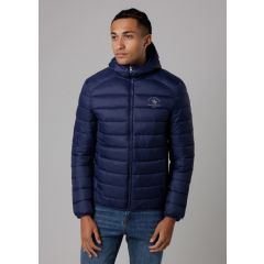 A person wearing a navy blue padded jacket with a hood stands against a plain gray background. They appear relaxed and are looking to the side.