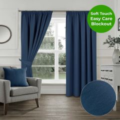 Navy blue soft touch blockout pencil pleat curtains styled in a white living room with a grey armchair and matching navy cushion