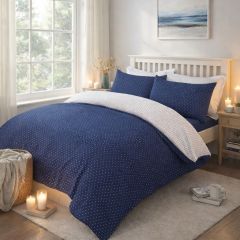 A neatly made bed with a blue and white polka dot duvet, matching pillows, in a bright room with a window and light wooden floor.