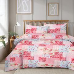 Quilted bedspread with red, pink, and blue floral patchwork design on a wooden bed, white walls, and abstract framed art.