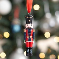 Nutcracker soldier ornament hanging on a decorated Christmas tree with festive lights in the background