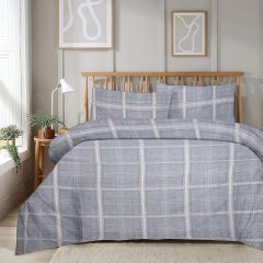 A neatly made bed with a gray plaid duvet in a bright room, featuring abstract wall art and a potted plant on a wooden side table.