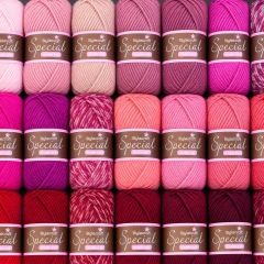 Rows of colorful Stylecraft Special yarn skeins in pink, coral, magenta, and red, neatly arranged with labels facing forward.