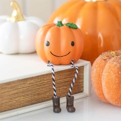 A small pumpkin figurine with a smiling face, rope legs, and boots sits on a book, surrounded by other decorative pumpkins.