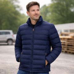 Man wearing a navy padded work jacket outdoors, standing with hands in pockets on a worksite background.